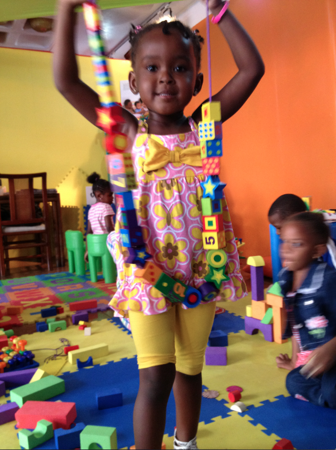 A basic school girl proudly shows the string of blocks she laced herself